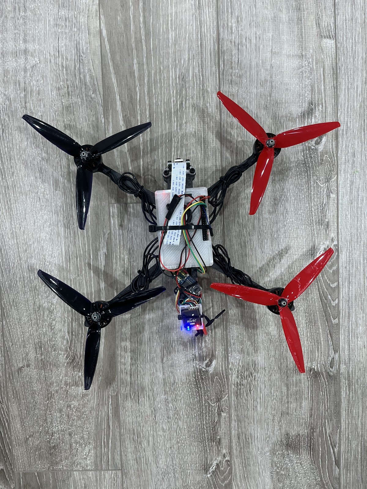 The quadcopter photographed from above: four three-blade propellers on a carbon frame, with the Raspberry Pi and wiring mounted over the flight-controller stack.