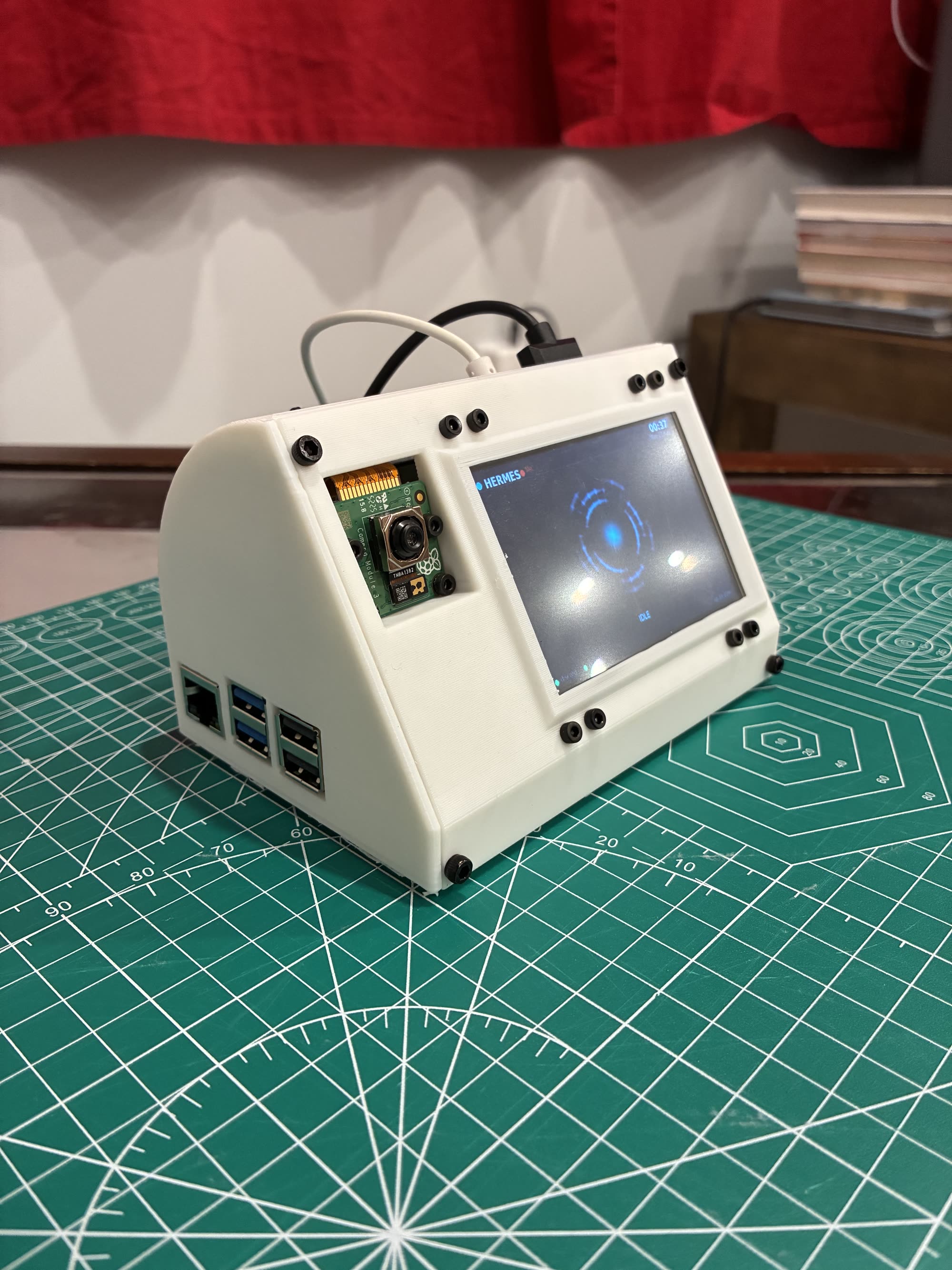The Hermes Pi from a front three-quarter angle, showing the wedge profile, the camera module, the lit panel, and the Raspberry Pi's ports along the lower side.